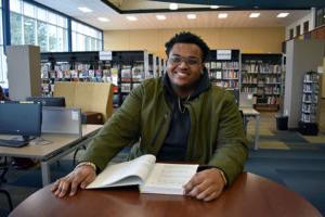 student sitting at table in library with book in front of him